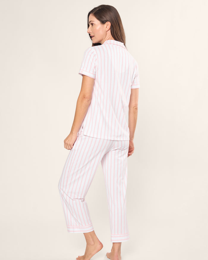 A woman stands barefoot in Petite Plumes Womens Pima Crop Set in Pink and White Stripe. Crafted from soft Pima cotton, she wears a short-sleeve button-up shirt and cropped pants against a plain off-white background.