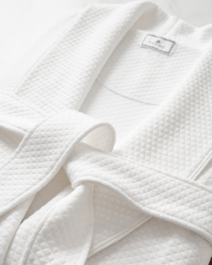 A close-up of the Womens Pima Ophelia Robe in White Jacquard by Petite Plume is laid flat, highlighting its luxurious quilted jacquard texture. The loosely tied belt and visible label enhance the robes elegance against a light, neutral background.
