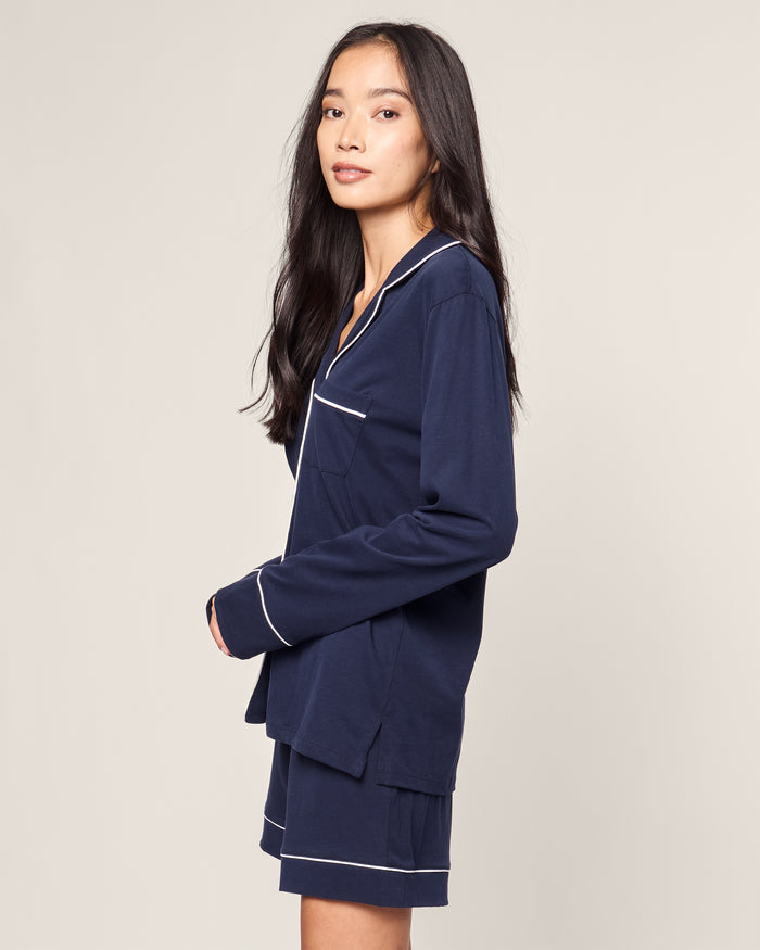 A person with long, dark hair is wearing the Petite Plume Womens Pima Long Sleeve Short Set in Navy, featuring white piping, and standing sideways against a plain background.