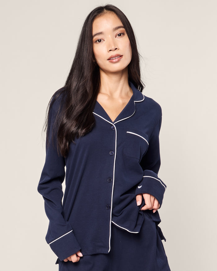 A woman with long dark hair wears Petite Plumes Womens Pima Long Sleeve Short Set in Navy, crafted from luxurious Peruvian Pima cotton with white piping. Her relaxed posture and gentle expression embody the essence of Classic PJs against a plain background.