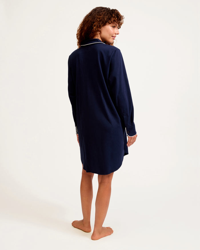 The Women's Pima Maternity Nightshirt in Navy features long sleeves, white piping on the collar, pocket, and cuffs, a chest pocket, button v-neckline, and a relaxed fit.