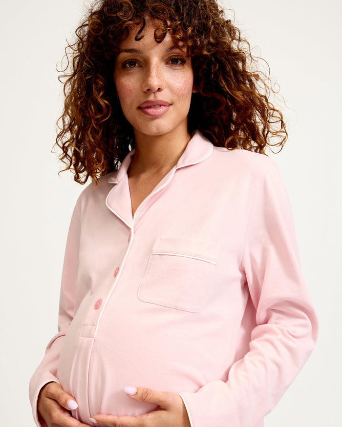 The Women's Pima Maternity Nightshirt in Pink features long sleeves, white piping, a collar, front buttons, single chest pocket, and a curved hem in soft, comfortable fabric.