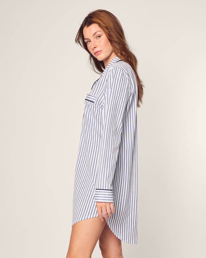A woman with long brown hair wears Petite Plumes Womens Pima Nightshirt in Navy French Ticking. Against a plain background, she looks over her shoulder, showcasing the comfort of this classic nightshirt made from Peruvian Pima cotton.