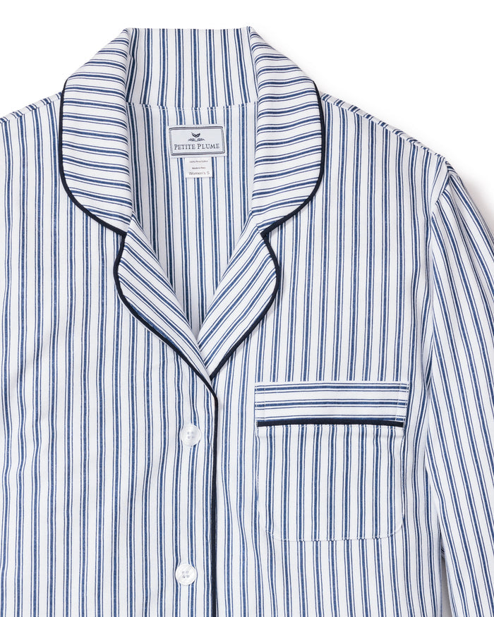 The Petite Plume Womens Pima Nightshirt in Navy French Ticking, crafted from luxurious Pima cotton, features a white and blue striped design with a collar, front pocket, black piping along the edges, and white buttons. The fabric label inside the collar highlights its premium quality.