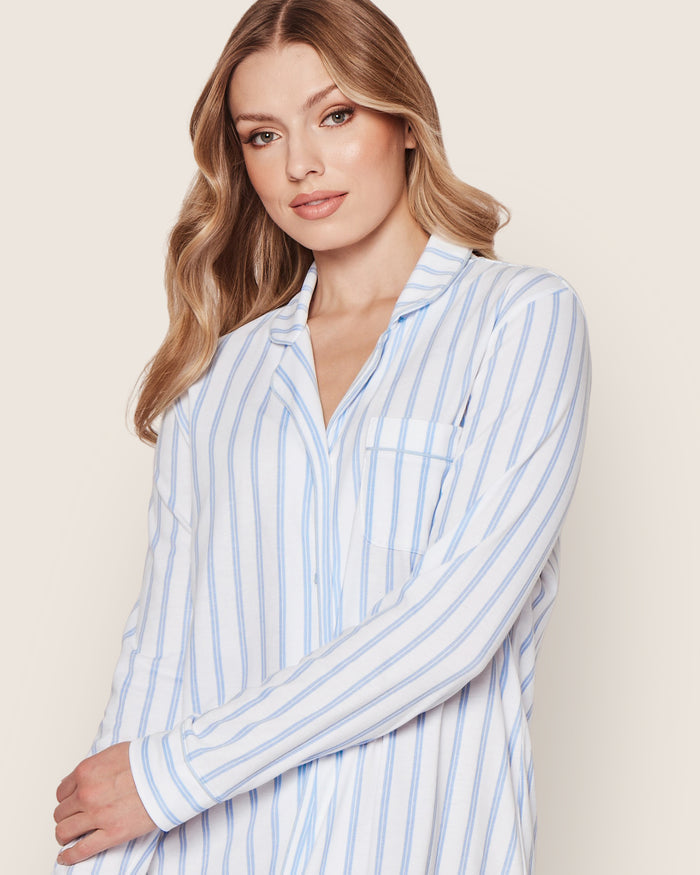 A woman with long, wavy blonde hair wears the Petite Plume Womens Pima Nightshirt in Periwinkle and White Stripe, standing against a plain light background and looking slightly to the side with a neutral expression.