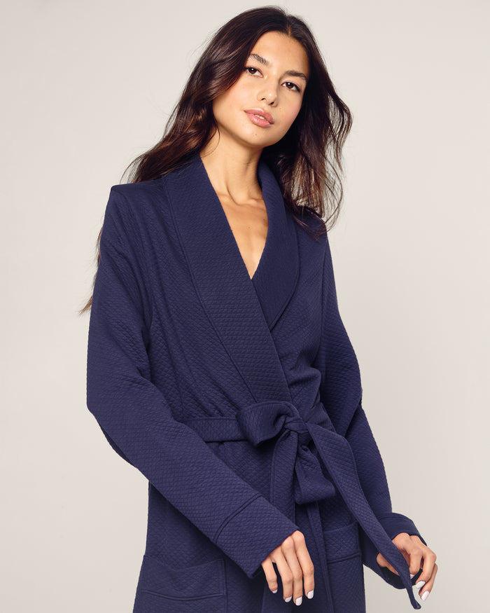 A woman with long dark hair wears the Petite Plume Womens Pima Ophelia Robe in Blue Dusk Jacquard, belted at the waist. She stands against a plain light background, looking slightly to the side with a neutral expression.