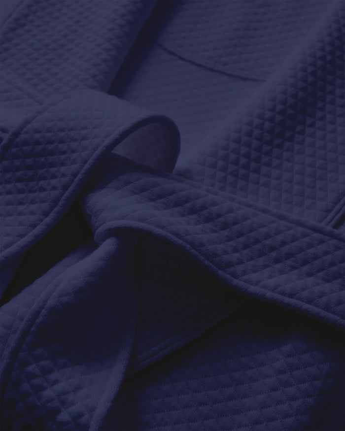 Close-up of the Womens Pima Ophelia Robe in Blue Dusk Jacquard by Petite Plume, highlighting its quilted pattern and tied belt. Made from Peruvian Pima cotton, the fabric looks soft and plush with folds adding depth and shadow.