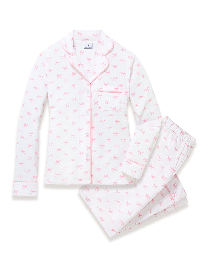 The Women's Pima Pajama Set in Blushing Bows features a long-sleeve button-up top and pants in white fabric with a small pink bow pattern and pink piping accents.