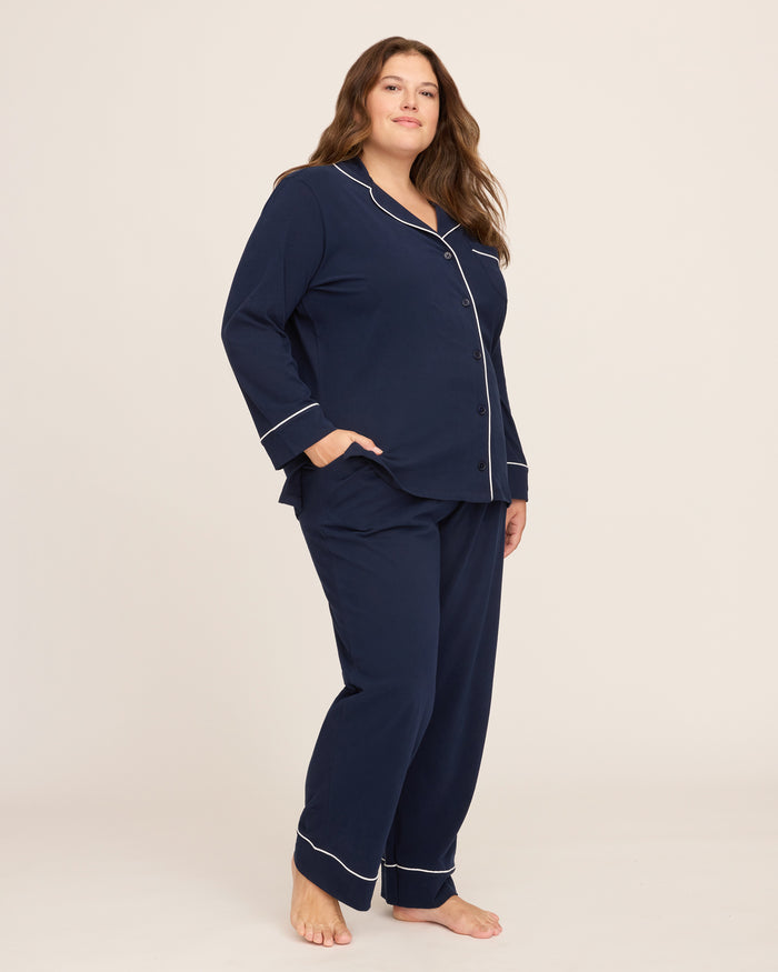 The Womens Pima Pajama Set by Petite Plume, in navy luxury sleepwear style, features white piping. This plus-size set includes a soft Pima cotton long-sleeve button-up top with a chest pocket and matching pants, displayed on a white background.