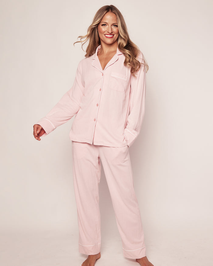 A person smiles while posing in the Womens Pima Pajama Set in Pink by Petite Plume. Made with soft Peruvian Pima cotton, this luxury sleepwear features a jersey knit button-up shirt with a collar and matching pants, set against a plain white background to highlight its texture.