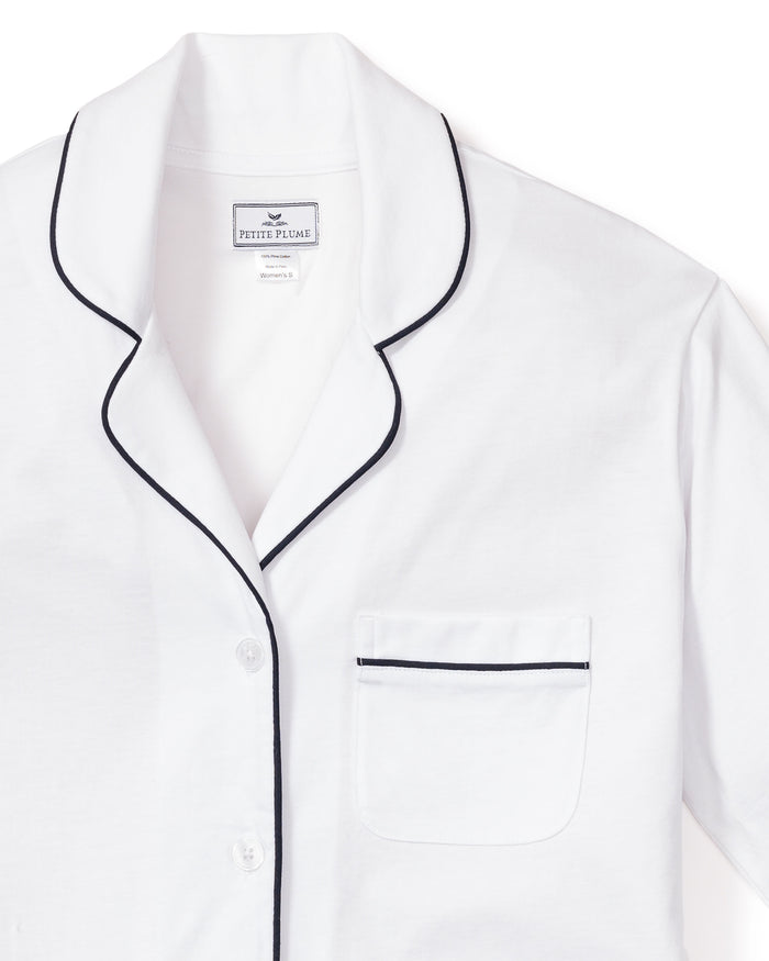 The Womens Pima Pajama Set by Petite Plume features a white top with navy piping, crafted from soft Peruvian Pima cotton. It includes a notched collar, button closure, and chest pocket for a classic design, ideal for luxury sleepwear enthusiasts.