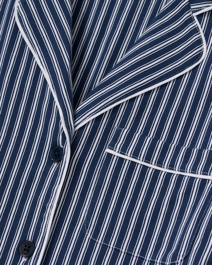 Close-up of the Women’s Pima Short Sleeve Short Set in Admiral Ticking, featuring a navy blue fabric with white vertical stripes, a notched lapel, buttons, and a chest pocket trimmed with white piping.