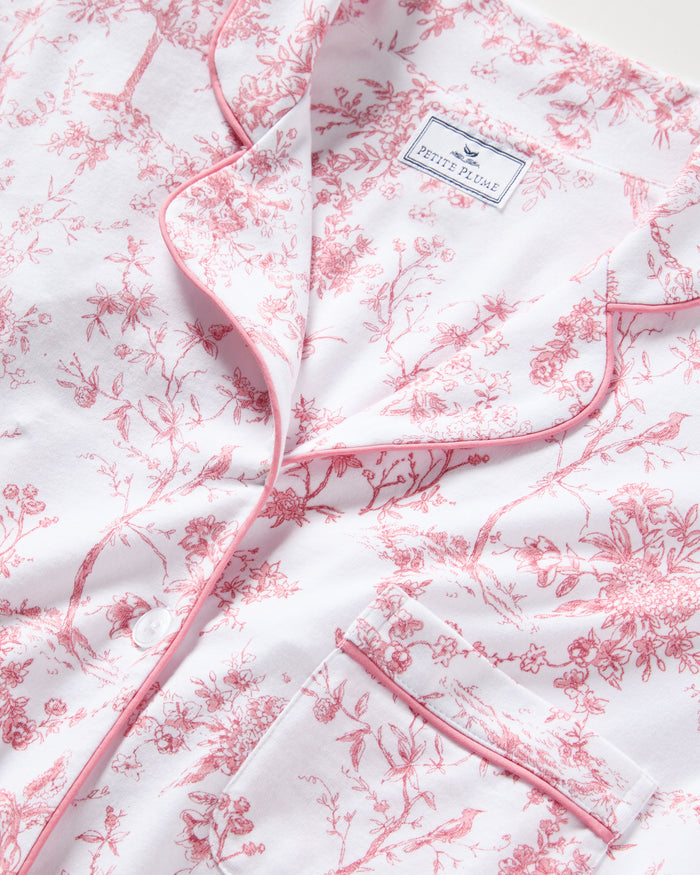 A close-up of the Womens Pima Short Sleeve Short Set in Pink Timeless Toile by Petite Plume showcases botanical elegance with a pink floral pattern and pink piping on the collar and pocket edges.