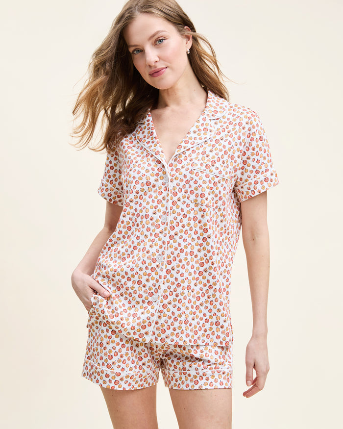 The Women's Pima Short Sleeve Short Set in Pumpkin Patch features a collared button-up top and matching shorts, both white with an orange and red fruit print and white piping on the edges.
