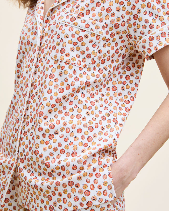 The Women's Pima Short Sleeve Short Set in Pumpkin Patch features a collared button-up top and matching shorts, both white with an orange and red fruit print and white piping on the edges.