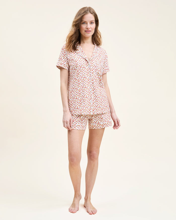 The Women's Pima Short Sleeve Short Set in Pumpkin Patch features a collared button-up top and matching shorts, both white with an orange and red fruit print and white piping on the edges.