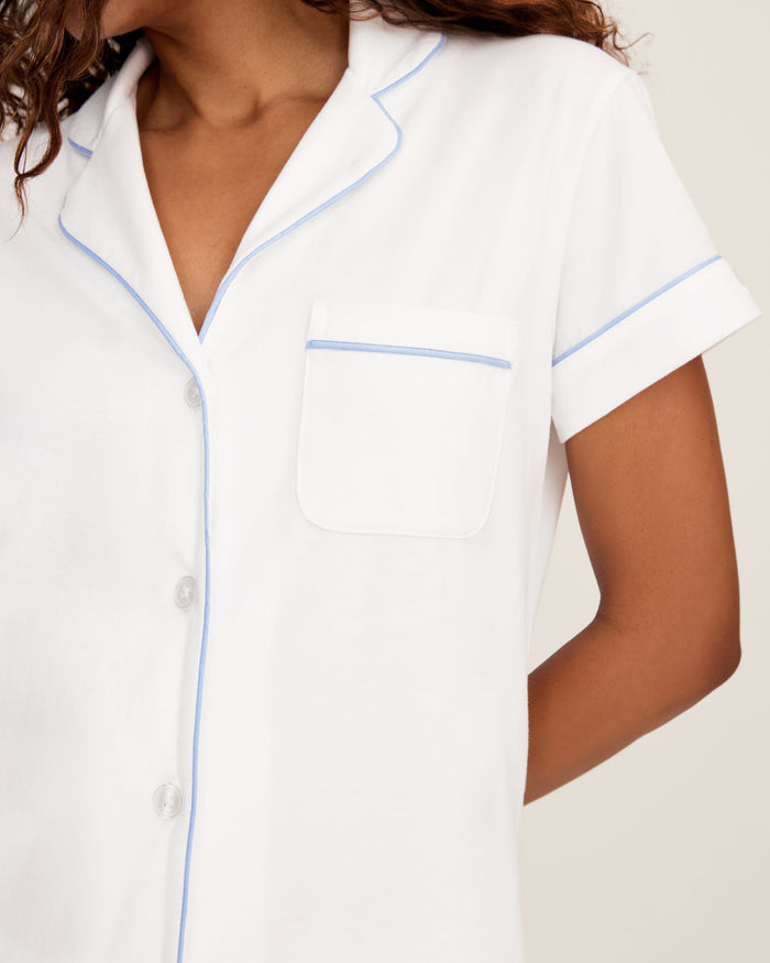 The Women's Pima Short Sleeve Short Set in White with Periwinkle Piping includes a collared button-up top with a chest pocket and matching shorts featuring an elastic waistband.