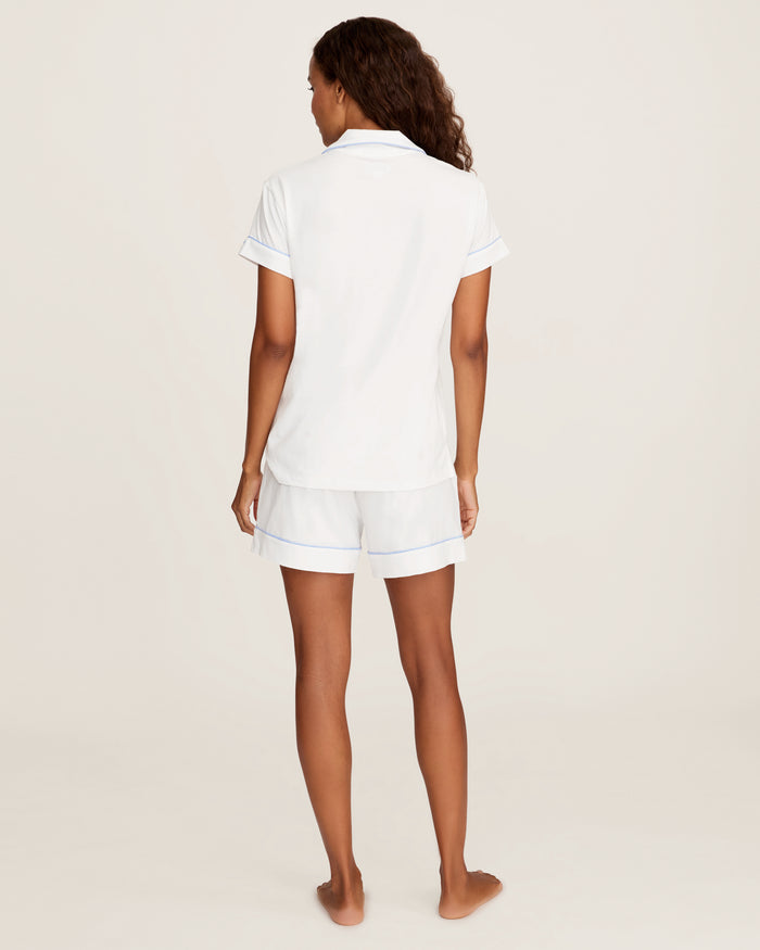 The Women's Pima Short Sleeve Short Set in White with Periwinkle Piping includes a collared button-up top with a chest pocket and matching shorts featuring an elastic waistband.