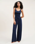 A woman with curly hair wears the Women's Pima Wide-Leg Lounge Pant in Navy and a matching tank top, standing barefoot against a plain light background and looking confidently at the camera.