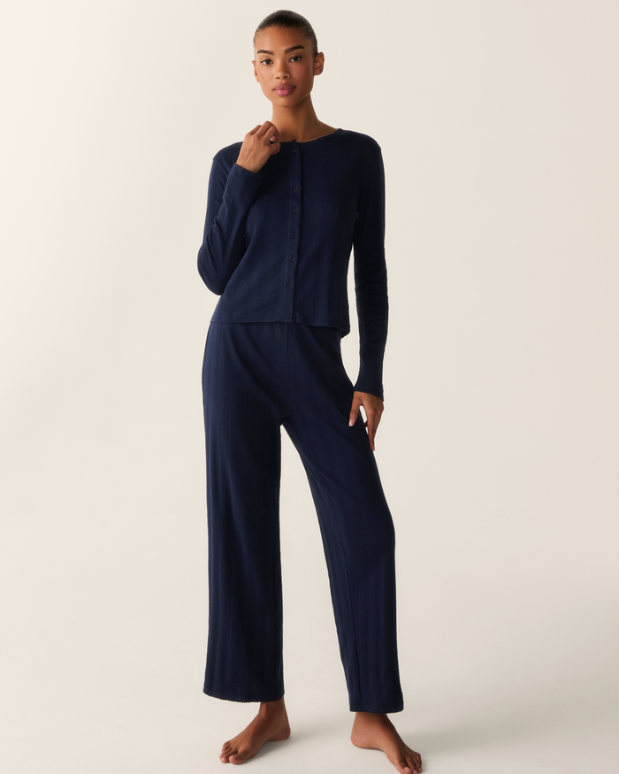 A person stands barefoot against a light background, wearing the Women’s Pointelle Cardigan in Navy paired with loose pants.
