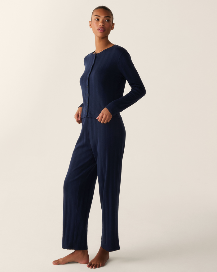 A woman stands barefoot against a plain background, wearing the Women’s Pointelle Cardigan in Navy.