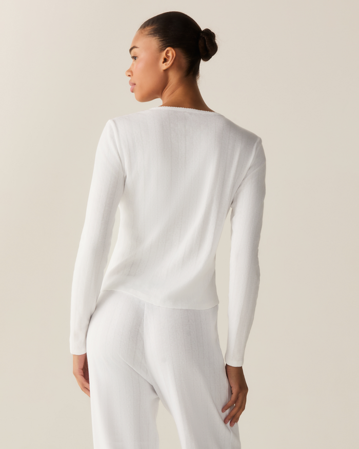 A woman with her hair in a bun models the Women’s Pointelle Cardigan in White, standing with her back to the camera against a light beige background.