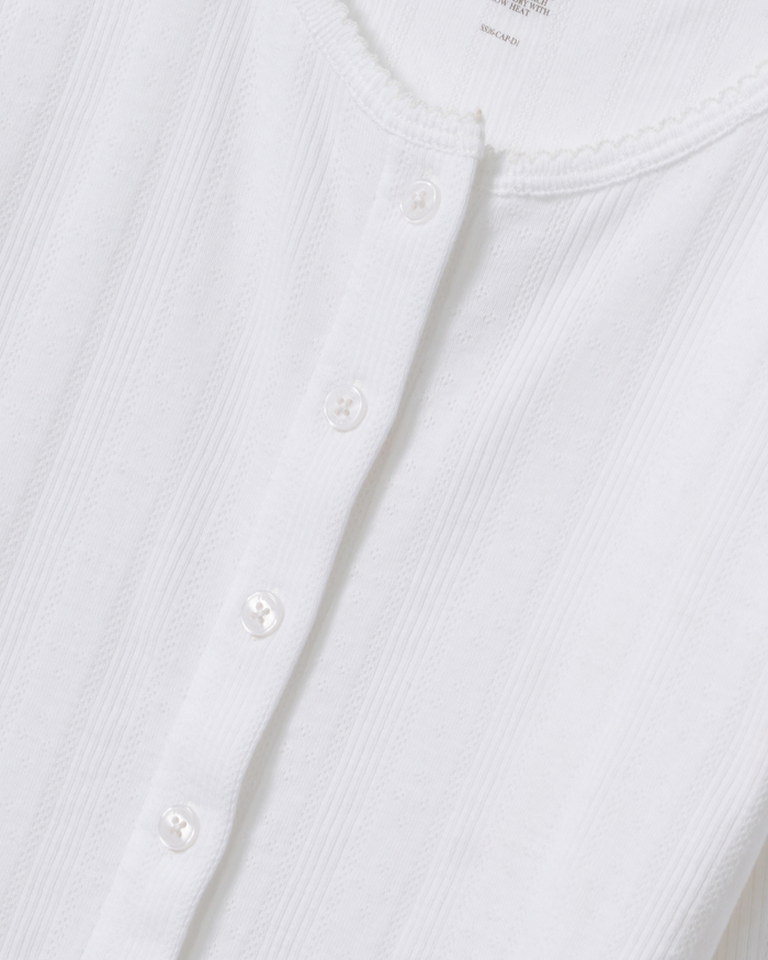 Close-up of the Women’s Pointelle Cardigan in White featuring a sleeveless, ribbed design with a button-down front. The cardigan has small white buttons, subtle vertical stripes in the fabric, and a round neckline finished with a delicate scalloped edge.
