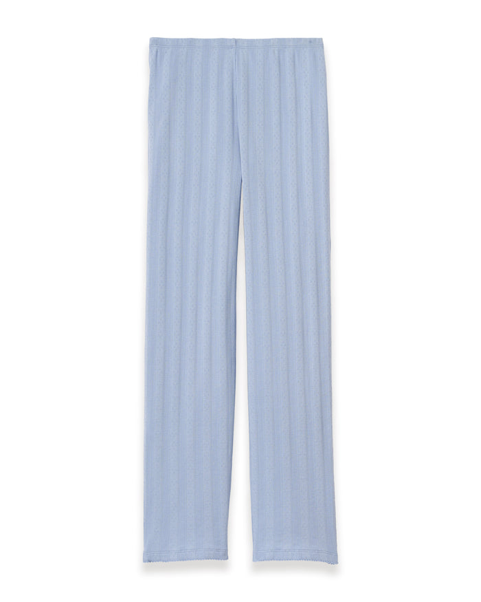 A woman stands barefoot in Women's Pointelle Pant in Periwinkle, paired with a matching short-sleeve top. She has wavy brown hair and gazes to the side against a plain, light background.