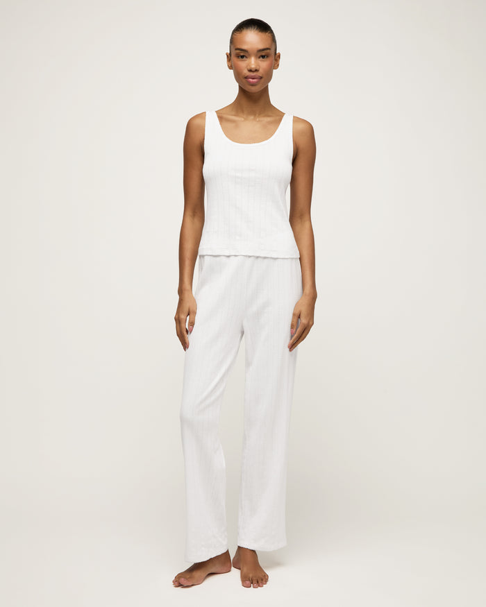 A woman stands barefoot on a light background wearing the Women's Pointelle Pant in White, paired with a sleeveless white tank top, posing with a relaxed and neutral expression.