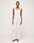 A woman stands barefoot on a light background wearing the Women's Pointelle Pant in White, paired with a sleeveless white tank top, posing with a relaxed and neutral expression.
