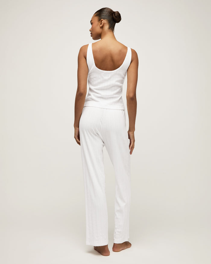 A woman stands barefoot on a light background wearing the Women's Pointelle Pant in White, paired with a sleeveless white tank top, posing with a relaxed and neutral expression.