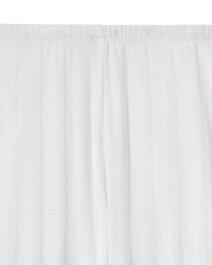 A woman stands barefoot on a light background wearing the Women's Pointelle Pant in White, paired with a sleeveless white tank top, posing with a relaxed and neutral expression.