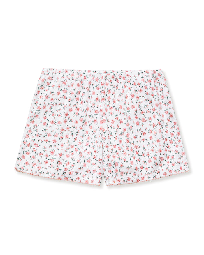 A woman with long curly hair and a relaxed expression stands barefoot against a neutral background, wearing Women's Pointelle Shorts in Pink Floral as part of a matching short-sleeved pajama set.