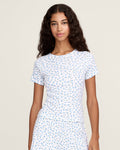 A young woman with long curly brown hair wears the Women's Pointelle T-Shirt in Blue Floral, paired with a matching skirt, against a plain light background.