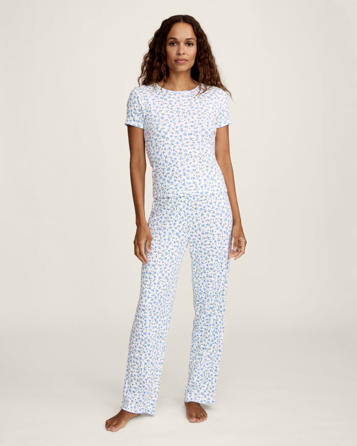 A young woman with long curly brown hair wears the Women's Pointelle T-Shirt in Blue Floral, paired with a matching skirt, against a plain light background.
