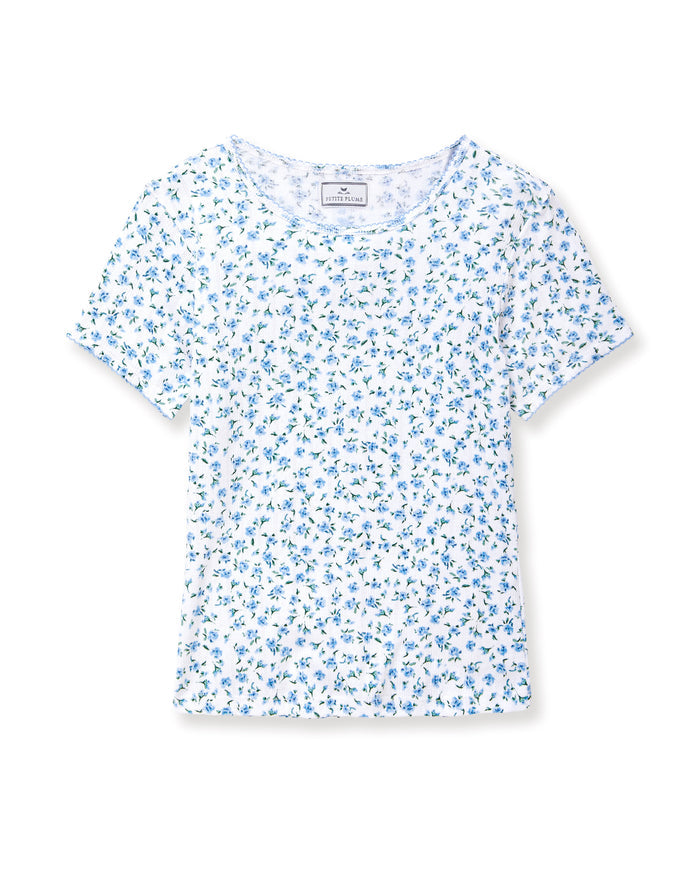 A young woman with long curly brown hair wears the Women's Pointelle T-Shirt in Blue Floral, paired with a matching skirt, against a plain light background.