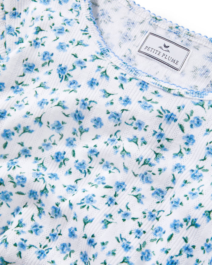 A young woman with long curly brown hair wears the Women's Pointelle T-Shirt in Blue Floral, paired with a matching skirt, against a plain light background.