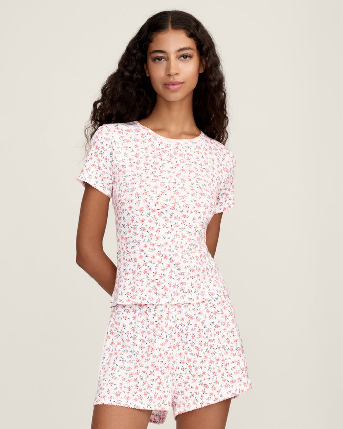 A woman with long curly hair wears the Women's Pointelle T-Shirt in Pink Floral, standing against a plain light background.