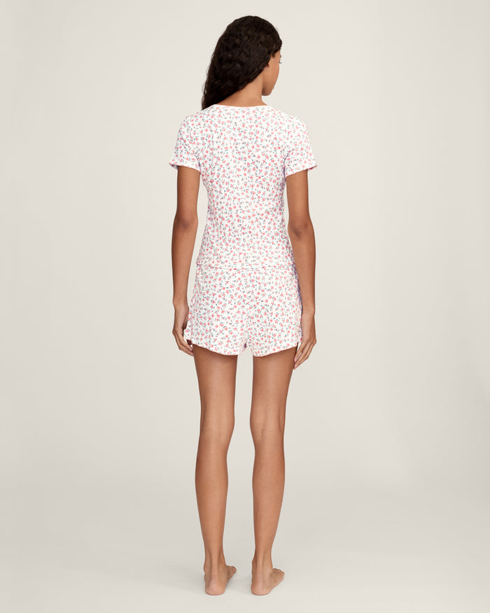 A woman with long curly hair wears the Women's Pointelle T-Shirt in Pink Floral, standing against a plain light background.