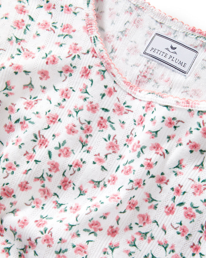 A woman with long curly hair wears the Women's Pointelle T-Shirt in Pink Floral, standing against a plain light background.