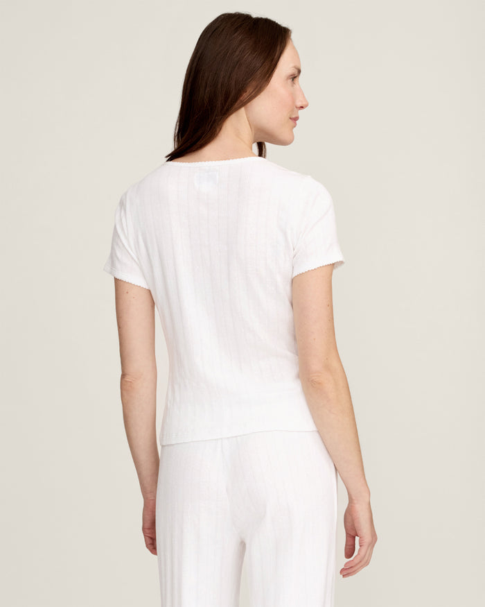 A woman with long brown hair wears the Women's Pointelle T-Shirt in White, standing against a plain light background and smiling gently at the camera.