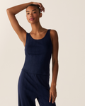 A woman wears the Women’s Pointelle Tank in Navy, paired with matching pants, as she stands against a neutral background. With one arm raised and resting on her head, she looks confidently at the camera.