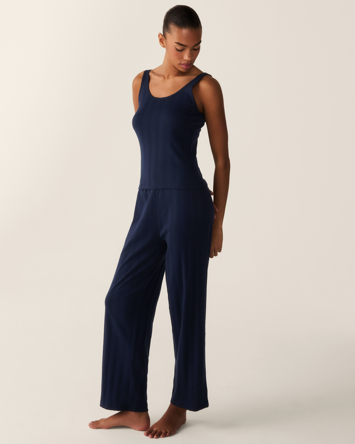 A woman stands barefoot, wearing the Women’s Pointelle Tank in Navy paired with wide-leg pants. She looks down and slightly to her side against a plain, light background.