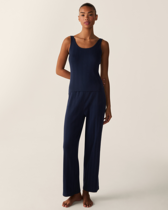 A woman stands barefoot on a light background, wearing the Women’s Pointelle Tank in Navy paired with matching wide-leg pants.