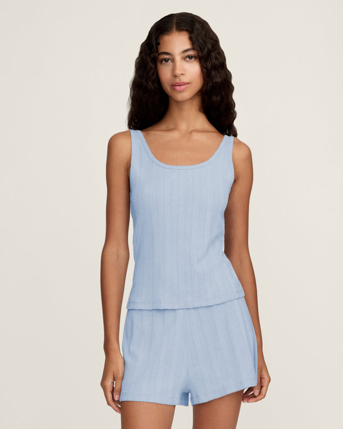 A woman with long wavy hair wears the Women's Pointelle Tank in Periwinkle, standing against a plain off-white background.