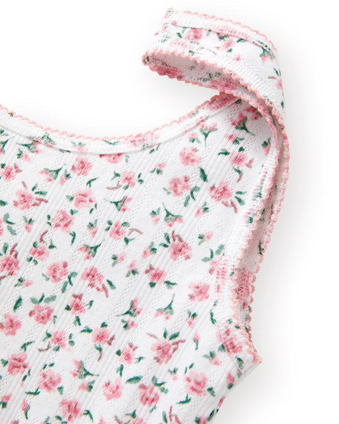 A woman with long brown hair smiles softly, wearing the Women's Pointelle Tank in Pink Floral with matching pants, standing against a plain light background.