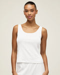 A woman with pulled-back hair wears the Women's Pointelle Tank in White and matching bottoms, standing against a plain light background and smiling softly at the camera.