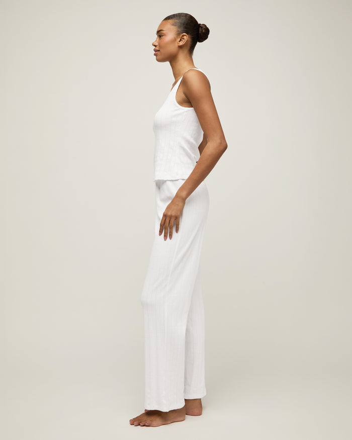 A woman with pulled-back hair wears the Women's Pointelle Tank in White and matching bottoms, standing against a plain light background and smiling softly at the camera.