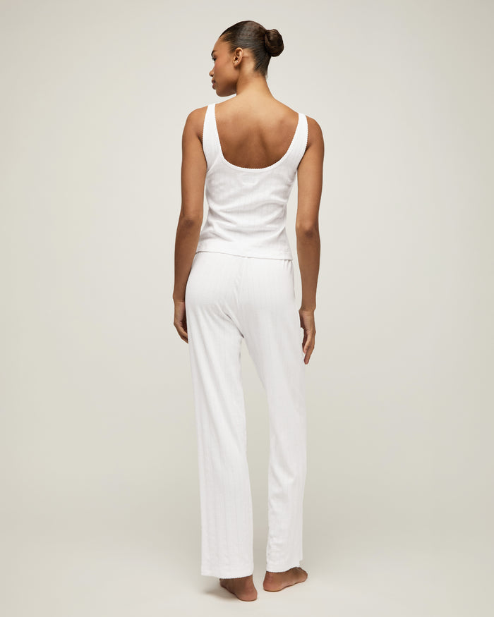 A woman with pulled-back hair wears the Women's Pointelle Tank in White and matching bottoms, standing against a plain light background and smiling softly at the camera.