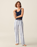 A woman stands barefoot wearing a navy tank top and the Women’s Poplin Romy Pants in Parlor Stripe against a plain light background.